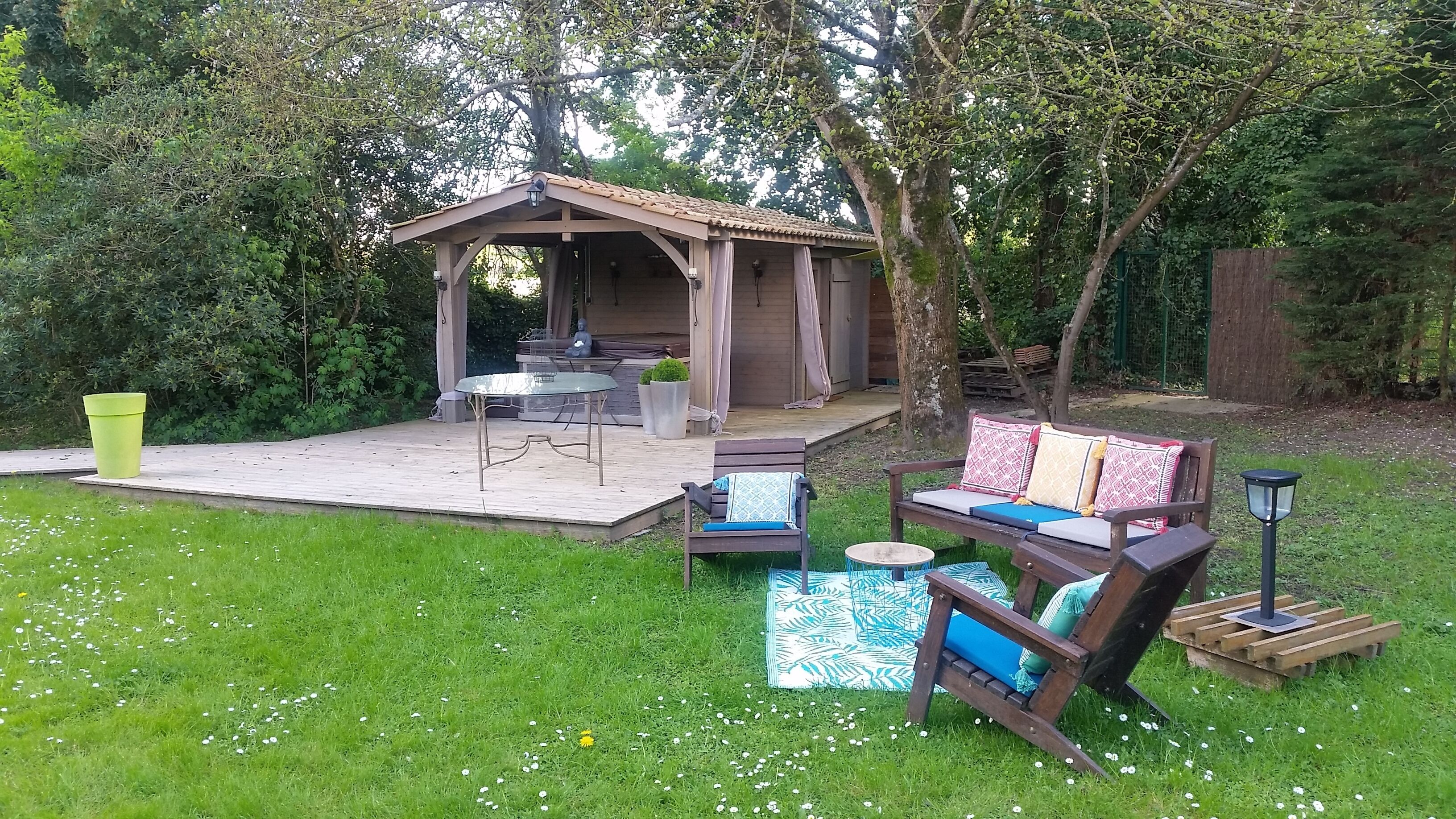 Een overdekt terras met een tafel en stoelen, omgeven door groen en een houten terras.