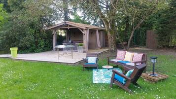 Een overdekt terras met een tafel en stoelen, omgeven door groen en een houten terras.