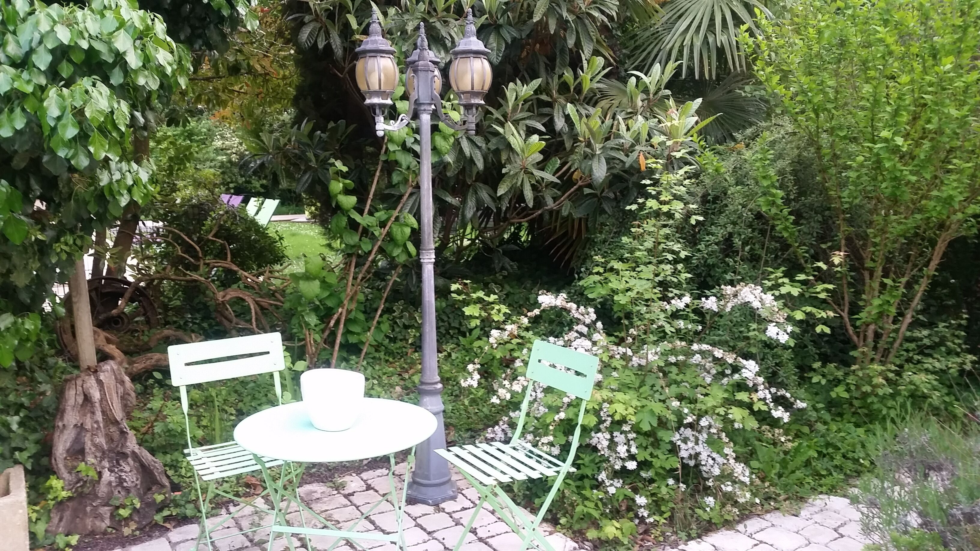 Un jardín con una mesa y sillas, rodeado de exuberante follaje y plantas con flores.