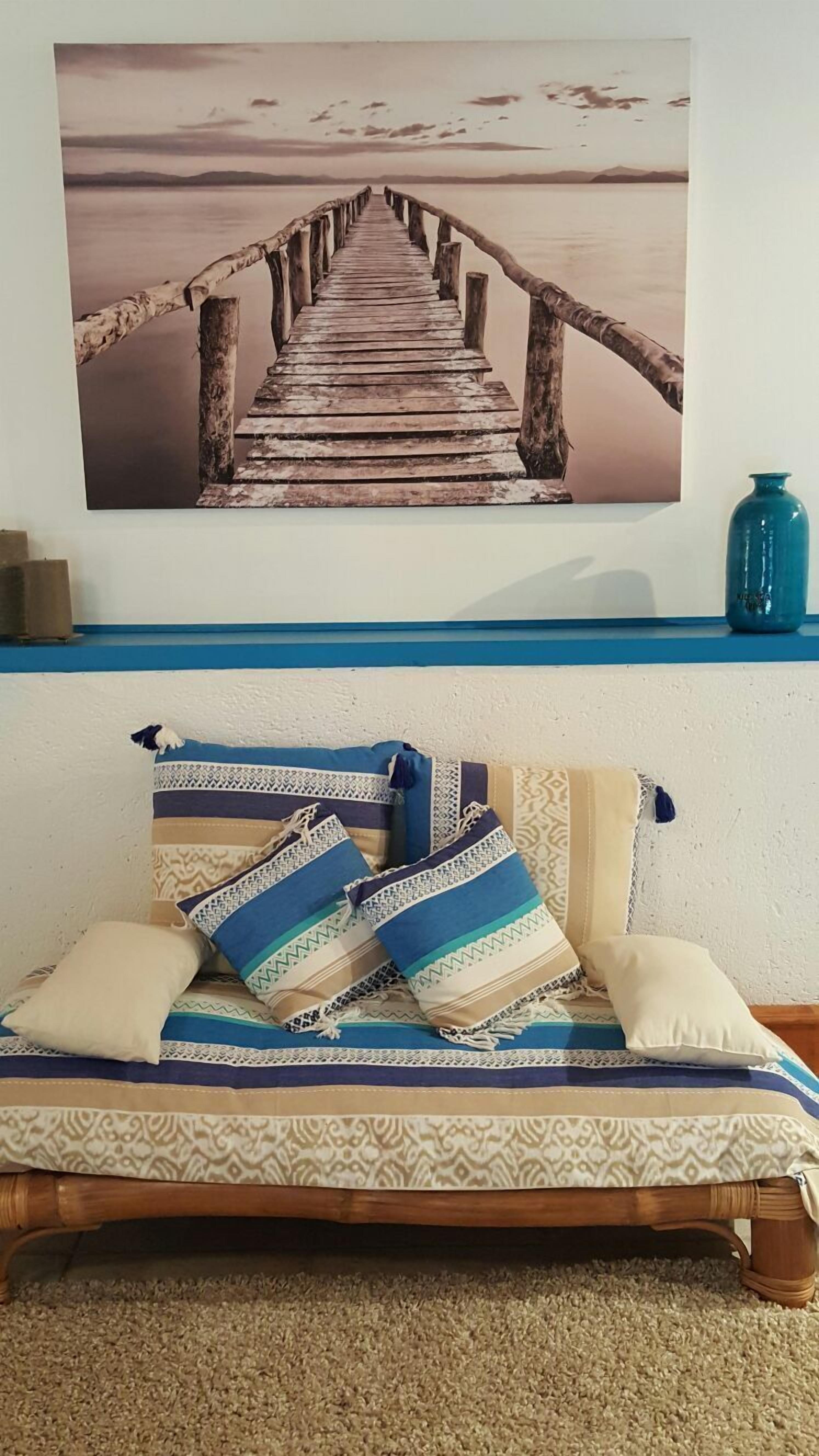 A bed with patterned bedding and pillows, a wooden headboard, and a wall-mounted picture of a wooden pier leading to a calm body of water.