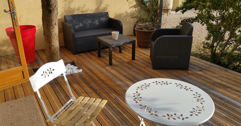 Un patio al aire libre con un sofá de mimbre, una mesita pequeña y una silla blanca.