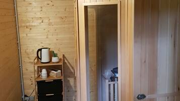 A wooden interior with a door leading to a room. There is a shelf with a kettle, a cactus, and a box.