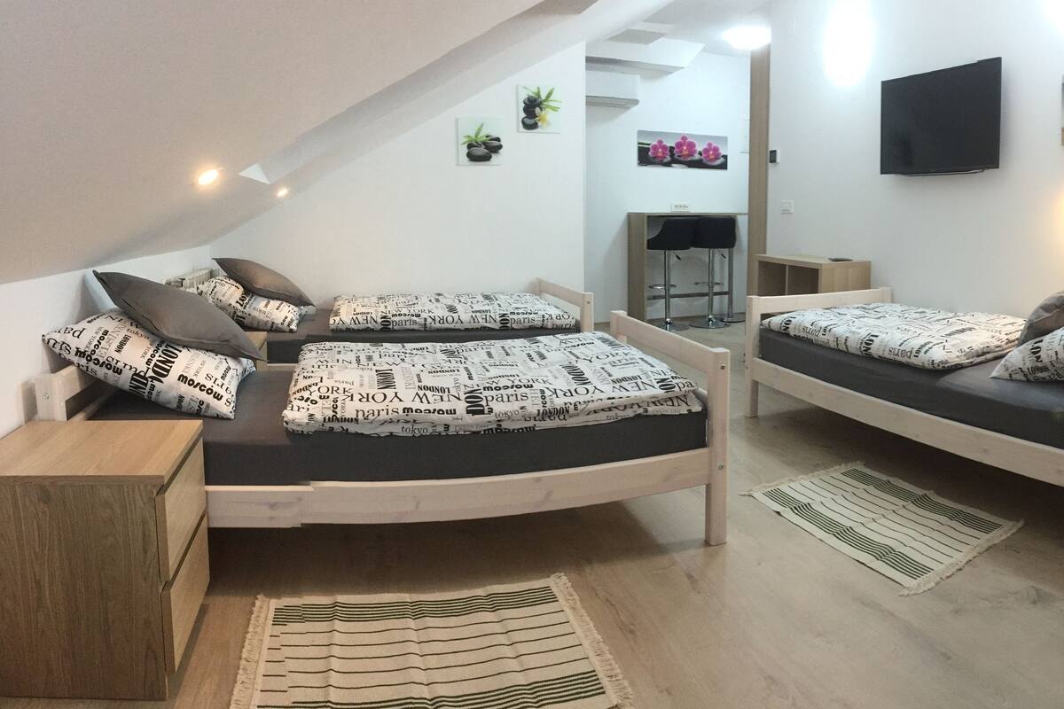 Un dormitori d'àtic acollidor amb dos llits superposats, cadascun amb roba de llit i coixins estampats. Hi ha un petit escriptori de fusta i una cadira, un televisor fixat a la paret i un quadre encimbellat sobre el llit.