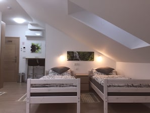 A bedroom with two single beds, a desk, a chair, a small table, a wall-mounted light, a picture of a waterfall, and a door. - Sobe-Rooms Kvatric (Zagreb)