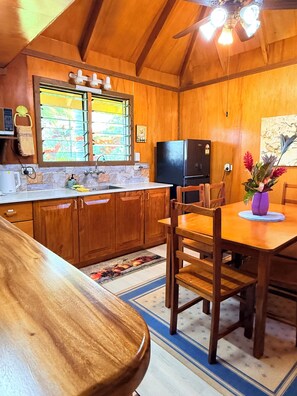 A wooden kitchen with a dining area, a refrigerator, and a ceiling fan. - Coco Cottage-Beachfront Romance or Budget Family (Savusavu)
