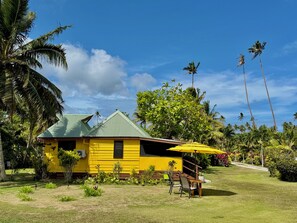A yellow building with a green roof, surrounded by palm trees and a well-maintained lawn. - Coco Cottage-Beachfront Romance or Budget Family (Savusavu)