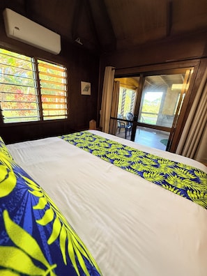 Ein Schlafzimmer mit einem großen Bett, einem Fenster mit Jalousien und Blick ins Freie.