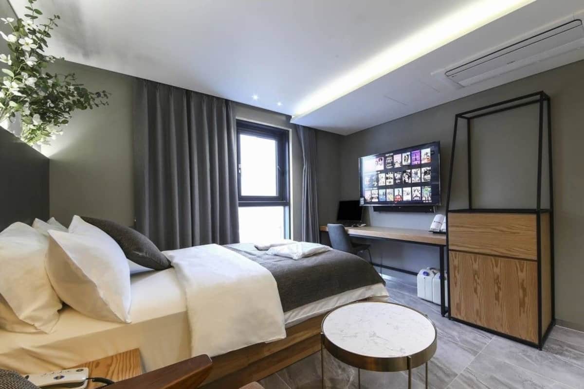 A modern hotel room with a bed, a desk, a TV, and a small round table.