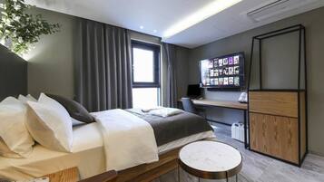 Una habitación de hotel moderna con una cama, un escritorio, un televisor y una pequeña mesa redonda.