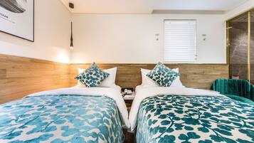 Habitación doble con dos camas, cada una con ropa de cama azul estampada, cabeceros de madera, mesitas de noche con teléfono y una ventana con persianas.