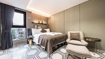 A modern hotel room with a large bed, a sitting area, and a view of the city through a large window.