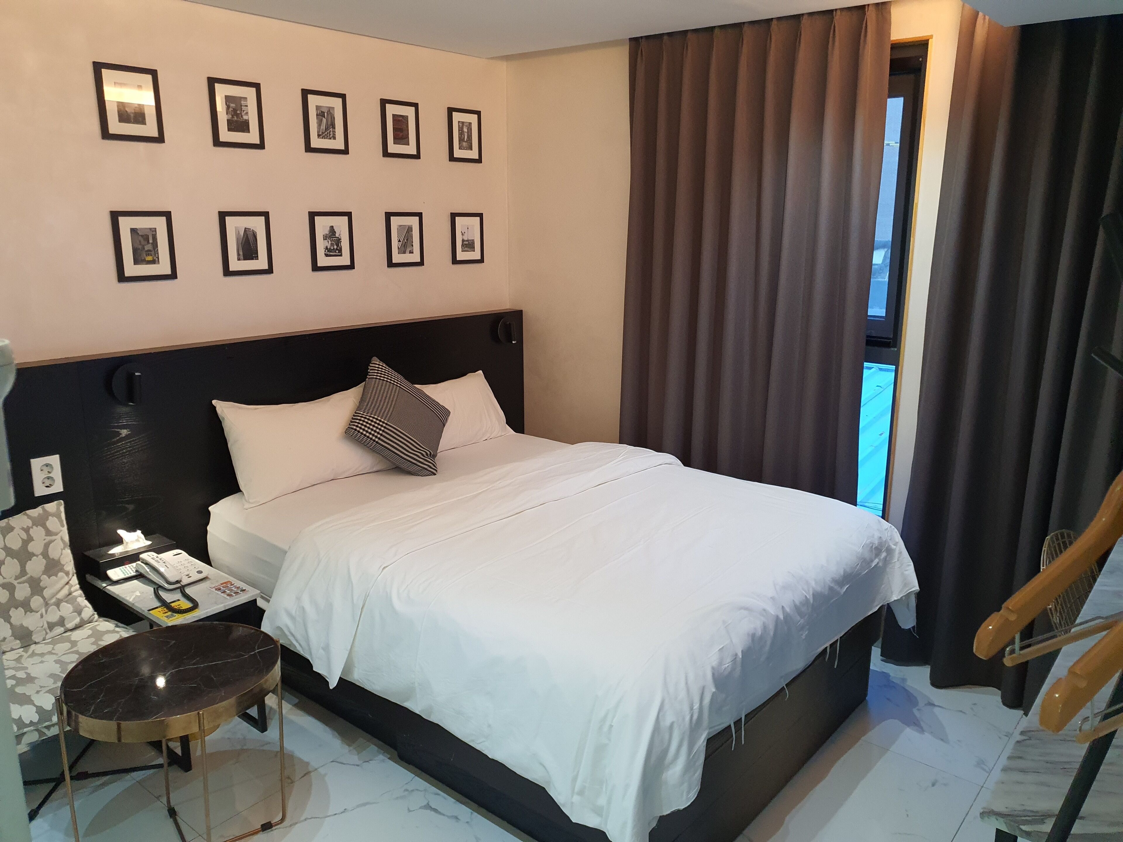 Habitación de hotel con cama, mesita de noche, silla y una pared con cuadros.