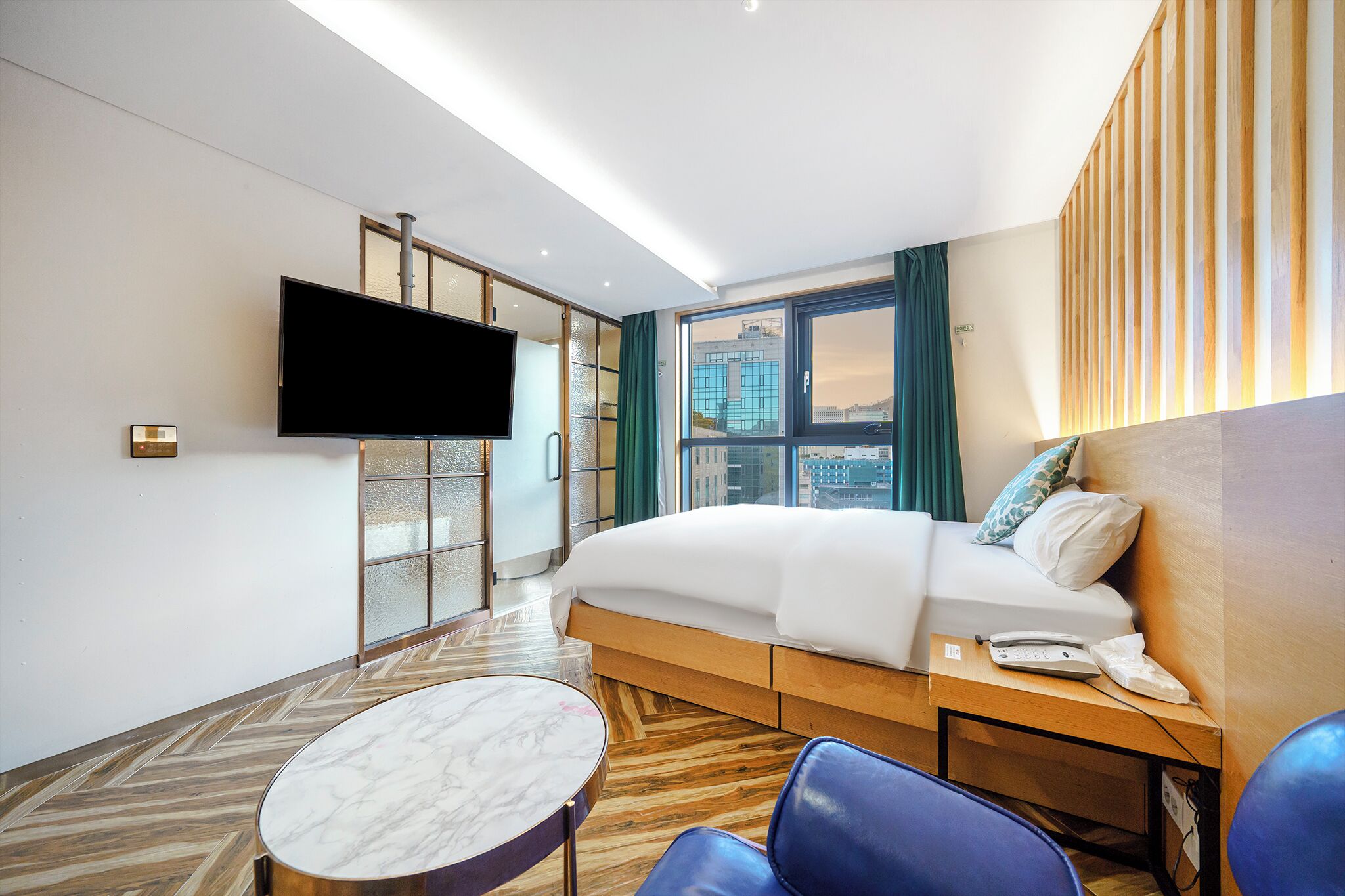 Habitación de hotel con cama, televisión, escritorio, silla y vista a la ciudad.