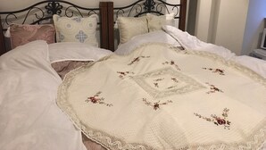 A neatly made bed with a floral-patterned quilt and lace trim, a metal headboard, and several pillows. - Guest House KAN (Tokyo)