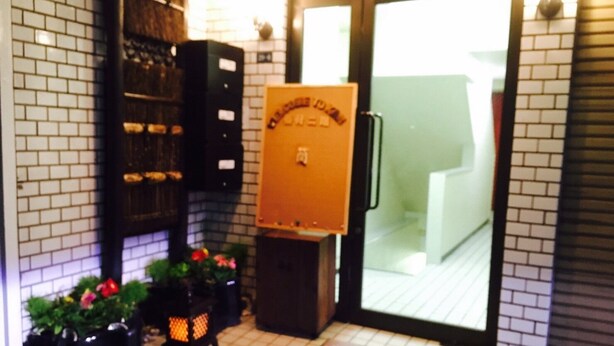 A hotel entrance with a tiled floor, a door with a sign, potted plants, and a small table with a placemat. - Guest House KAN (Tokyo)