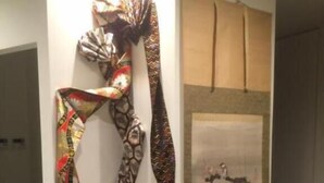 A room with a white wall, a framed artwork, a potted plant with purple flowers, and a patterned scarf hanging on the wall. - Guest House KAN (Tokyo)