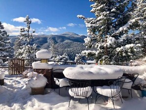 Un espace extérieur aménagé avec des tables et des chaises, recouvert de neige, entouré d’arbres chargés de neige et avec une montagne en toile de fond.