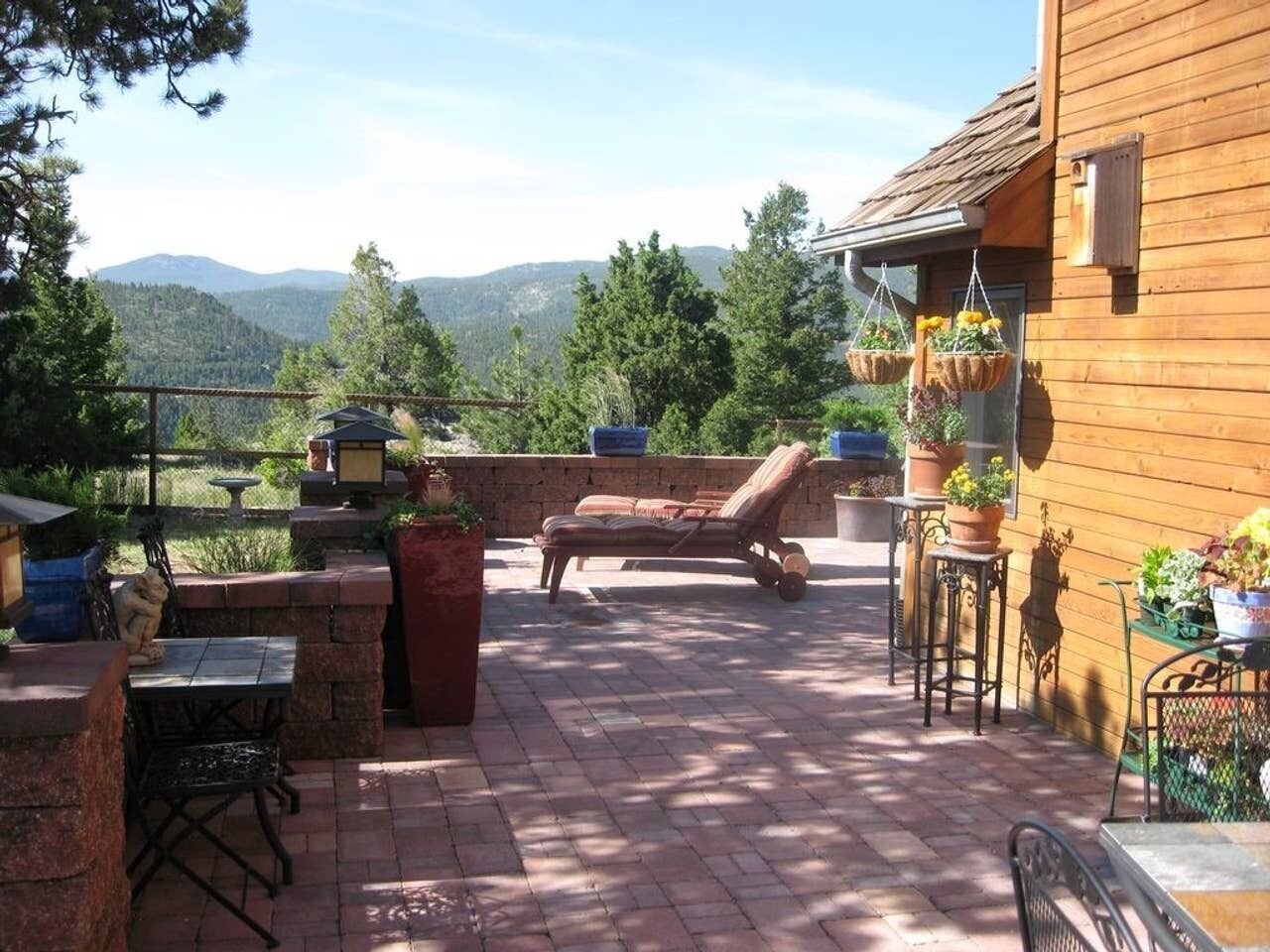 A patio with a brick floor, a lounge chair, a table, and hanging flower baskets.