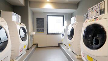 Une buanderie équipée de plusieurs machines à laver et de plusieurs sèche-linge, avec une fenêtre et des panneaux d’information.