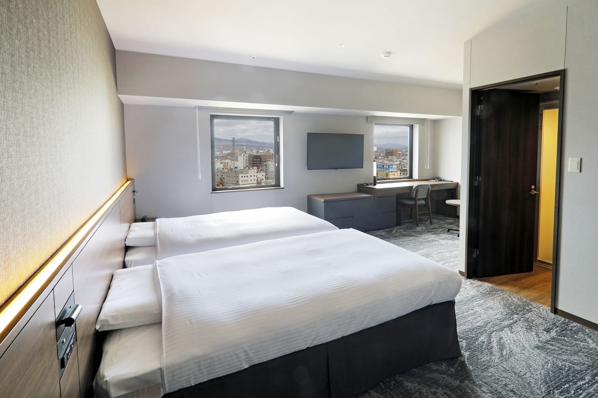 Quarto de hotel com cama, escrivaninha, cadeira, televisão e vista para a cidade.