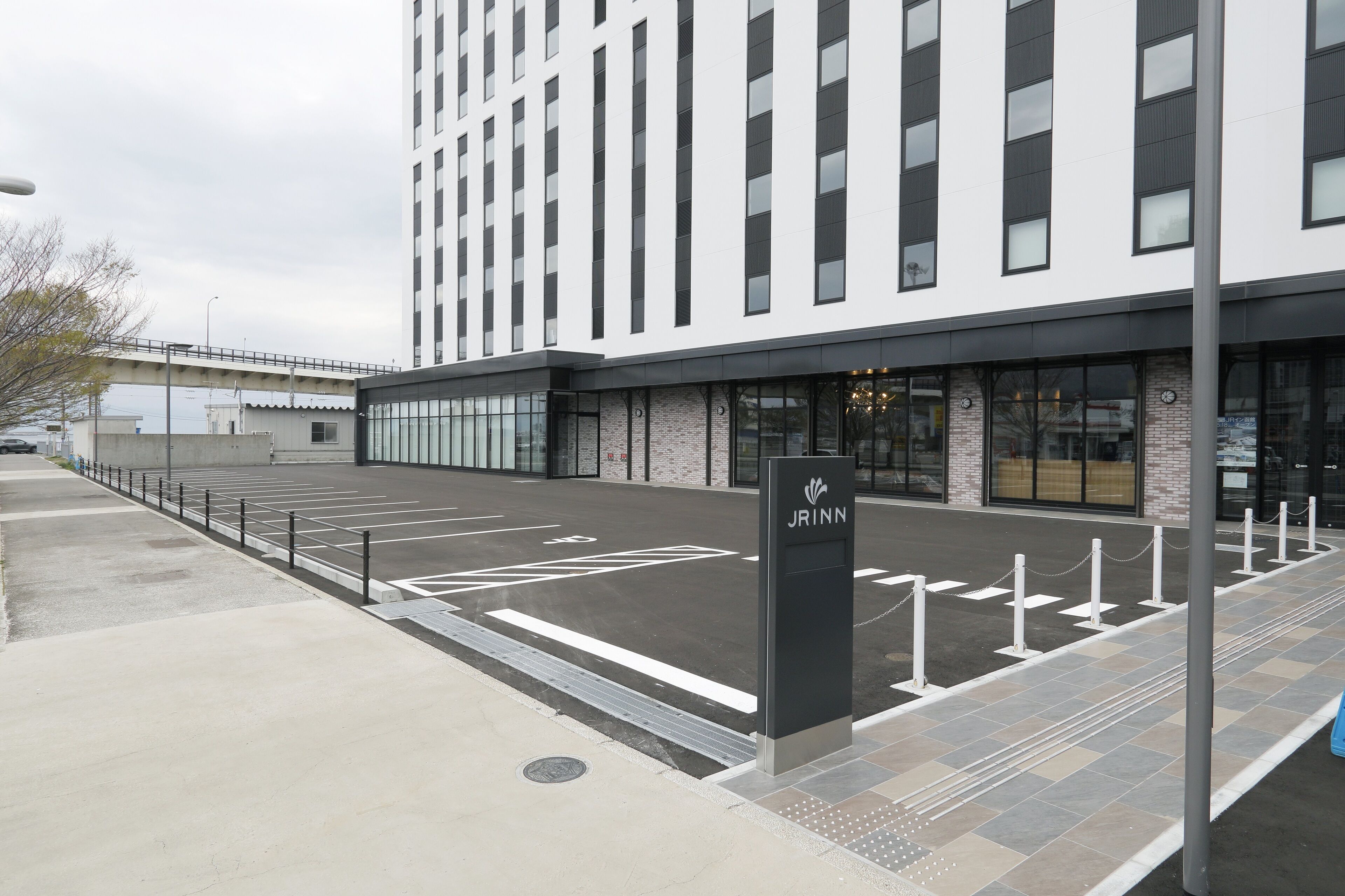 A modern building with a parking lot, a pedestrian pathway, and a sign with the name "JRINN".