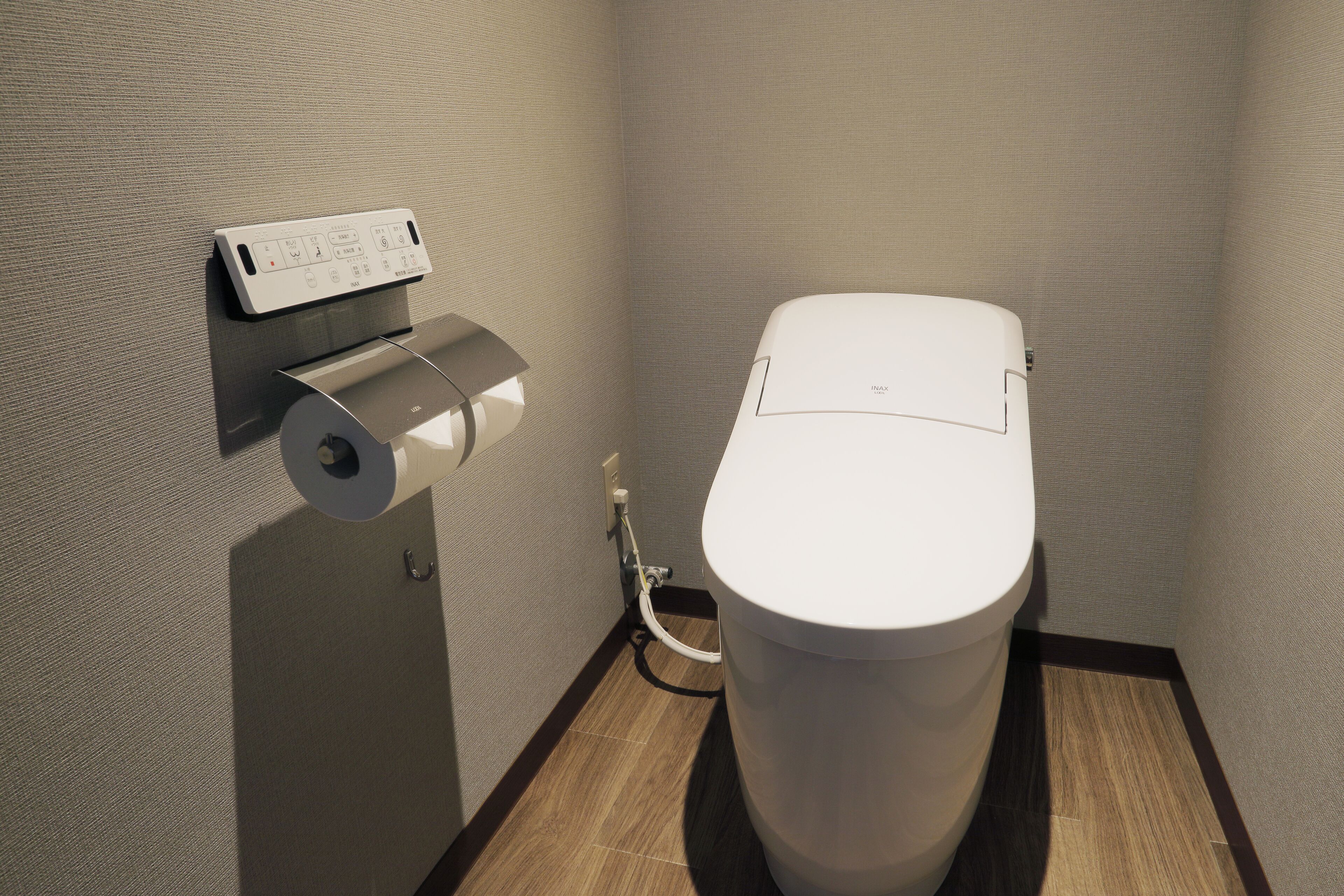A modern bathroom with a toilet, a wall-mounted paper towel dispenser, and a visible toilet paper roll.