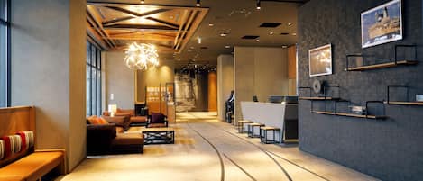 A modern hotel lobby with a reception desk, seating area, and artwork on the walls.