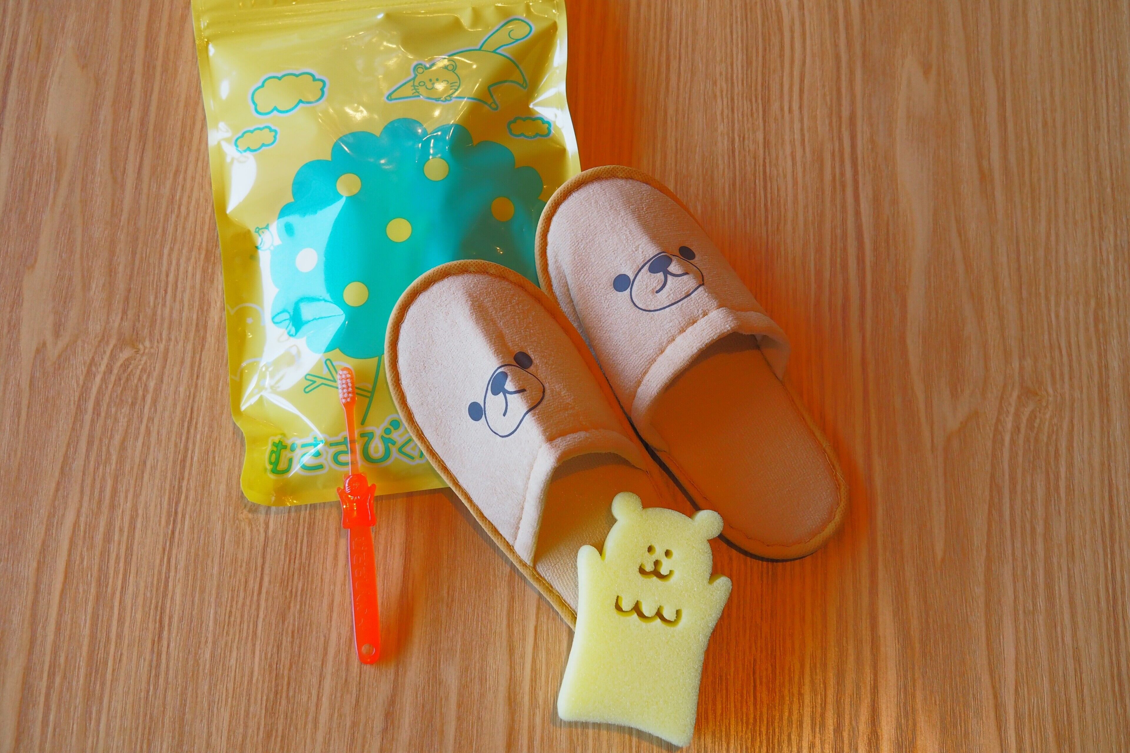 A pair of slippers, a small toy, and a toothbrush on a wooden surface.