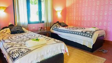 Una habitación con dos camas, cada una con ropa de cama y almohadas estampadas, una mesita de noche con lámpara y una ventana con cortinas.