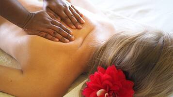 Eine Person bekommt eine Rückenmassage auf einem Bett, verziert mit einer roten Blütenaccessoire.
