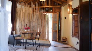 A room with a wooden ceiling, a bamboo partition, a round table with chairs, and a small basket. - Sapana Village Lodge (Sauraha)