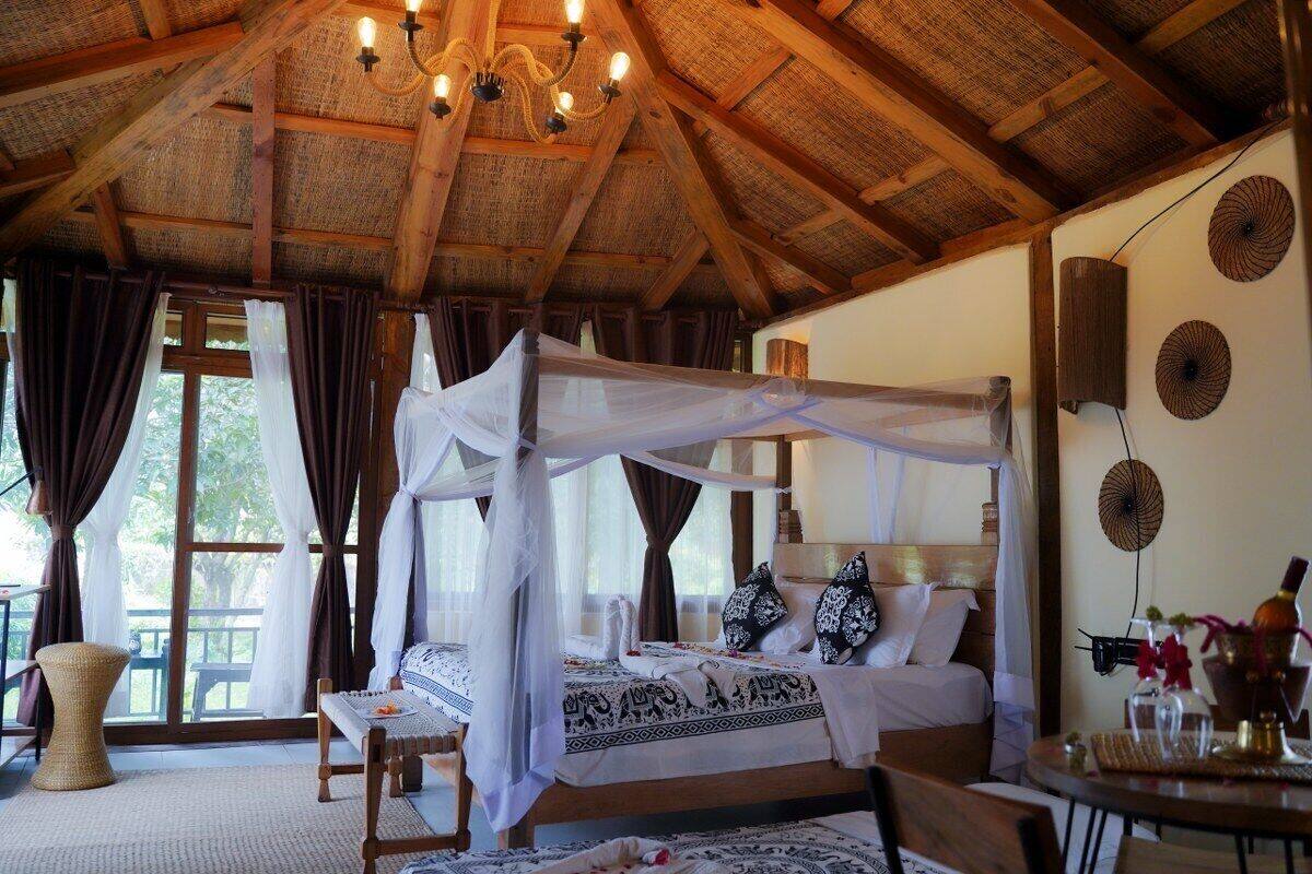 A room with a bed under a canopy, a wooden ceiling, and a view of greenery outside.