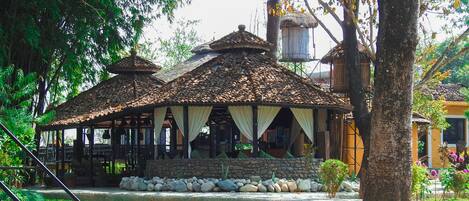 A traditional wooden structure with a tiled roof, stone walls, and a thatched roof building in the background.