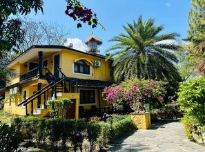 A yellow building with a staircase, a thatched-roof structure, and a palm tree. - Sapana Village Lodge (Sauraha)