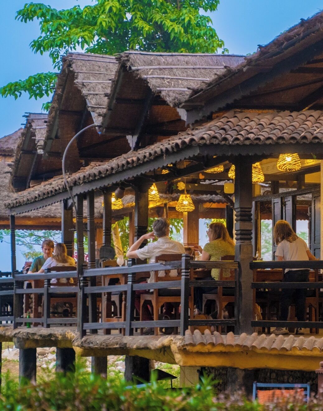 A traditional wooden structure with a balcony, featuring a thatched roof and hanging lights.