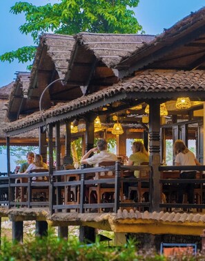 A traditional wooden structure with a balcony, featuring a thatched roof and hanging lights. - Sapana Village Lodge (Sauraha)
