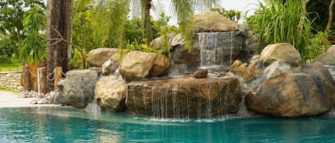 Una piscina con una cascada rodeada de rocas grandes y palmeras.