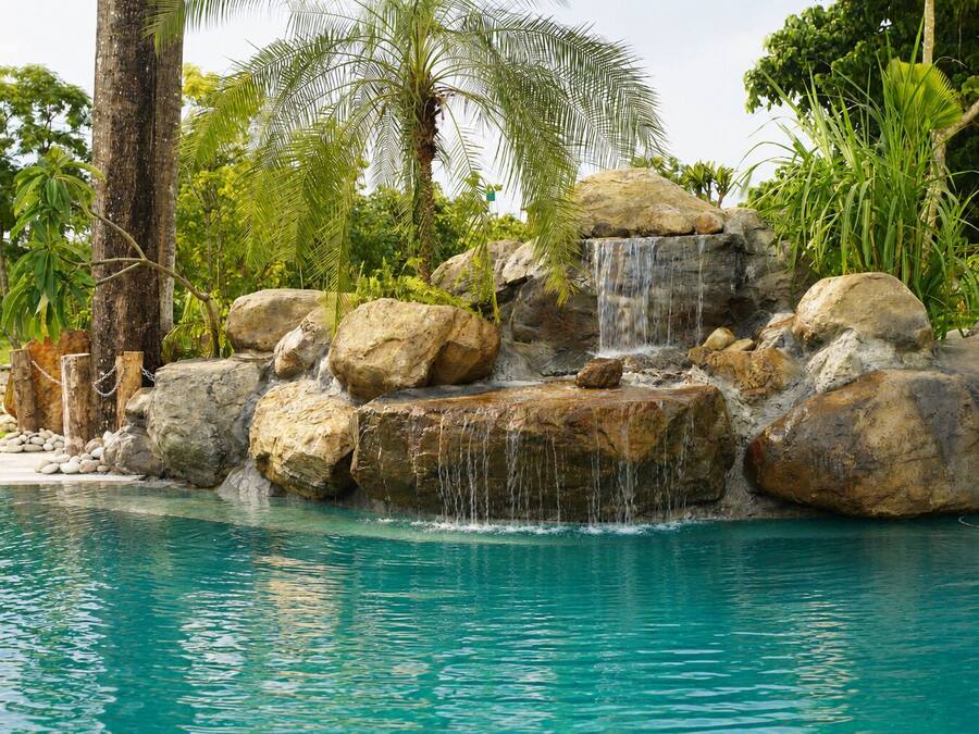 A pool with a waterfall feature surrounded by large rocks and palm trees.