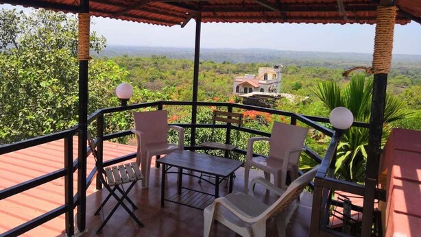 A covered outdoor seating area with a table and chairs, overlooking a lush landscape and a distant building.