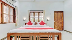 A bedroom with a wooden bed, two red pillows, a white bedspread, and a wooden door.