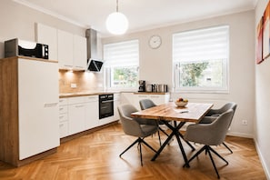 Een moderne keuken met witte kastjes, een inbouwoven en een eettafel met vier stoelen.