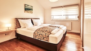 Un dormitorio ordenado con cama, mesita de noche, lámpara y ventana con persianas.
