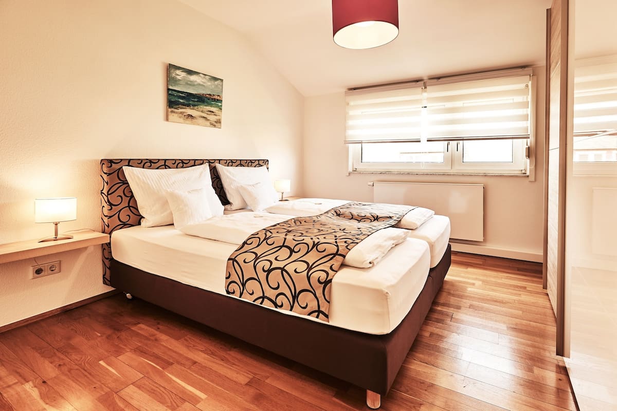 Une chambre à coucher bien rangée, avec un lit, une table de chevet, une lampe et une fenêtre équipée de stores.
