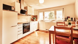 Una cocina moderna con armarios blancos, horno empotrado y comedor con sillas y mesa de madera.