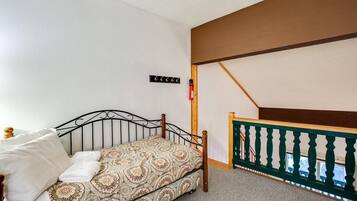 A single bed with a patterned bedspread, a wooden headboard, and a small bedside table with a lamp. A fire extinguisher is mounted on the wall.