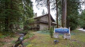 A lodge with a stone sign, surrounded by dense forest and a small stream. - 56SLL - Fireplace - Inexpensive - Kitchenette - Sleeps 4 (Deming)