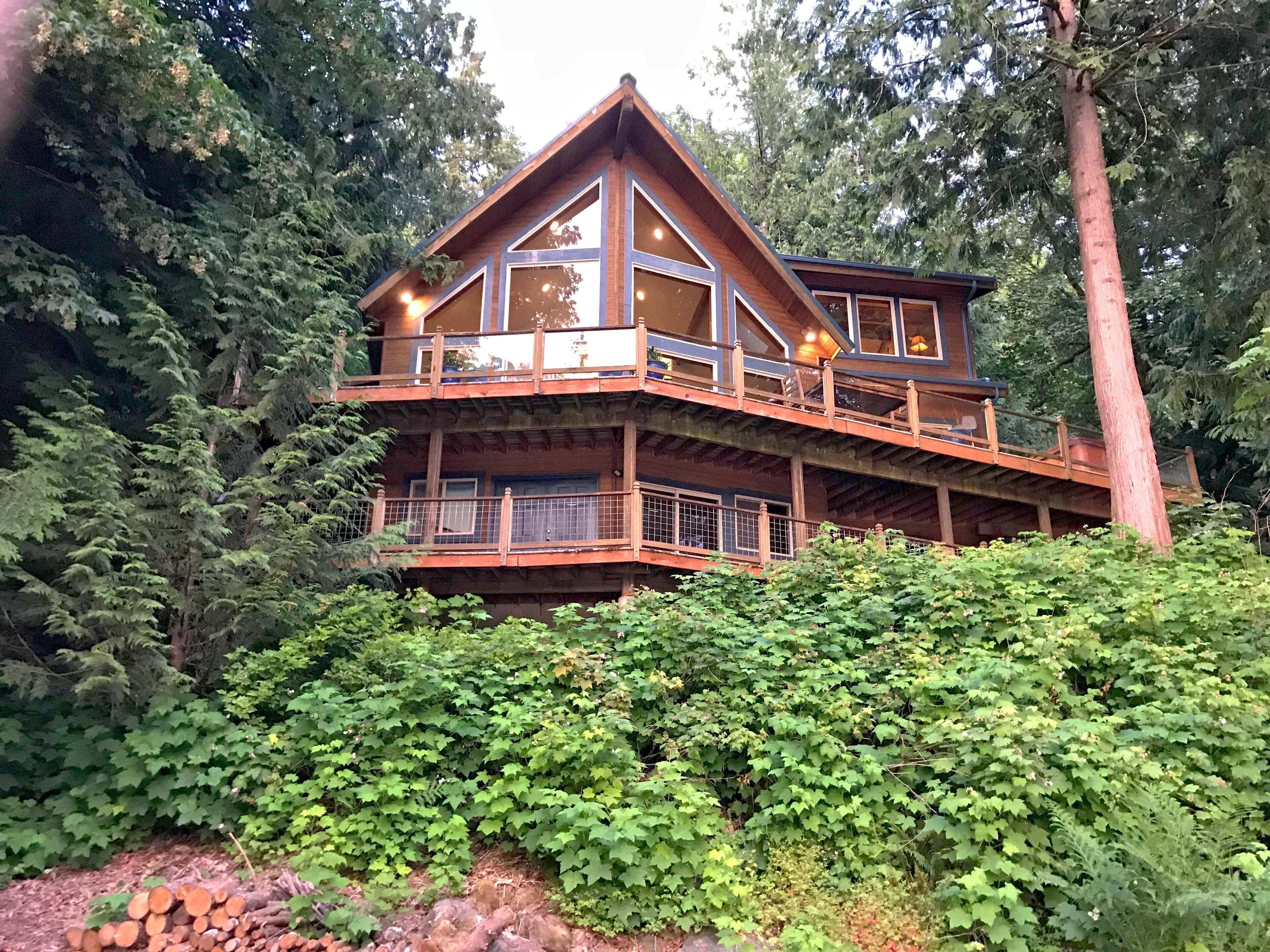 A multi-level wooden cabin with balconies, surrounded by dense forest.