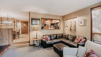 A modern living room with a leather sectional sofa, a white armchair, and a dining area with a wooden table and chairs.