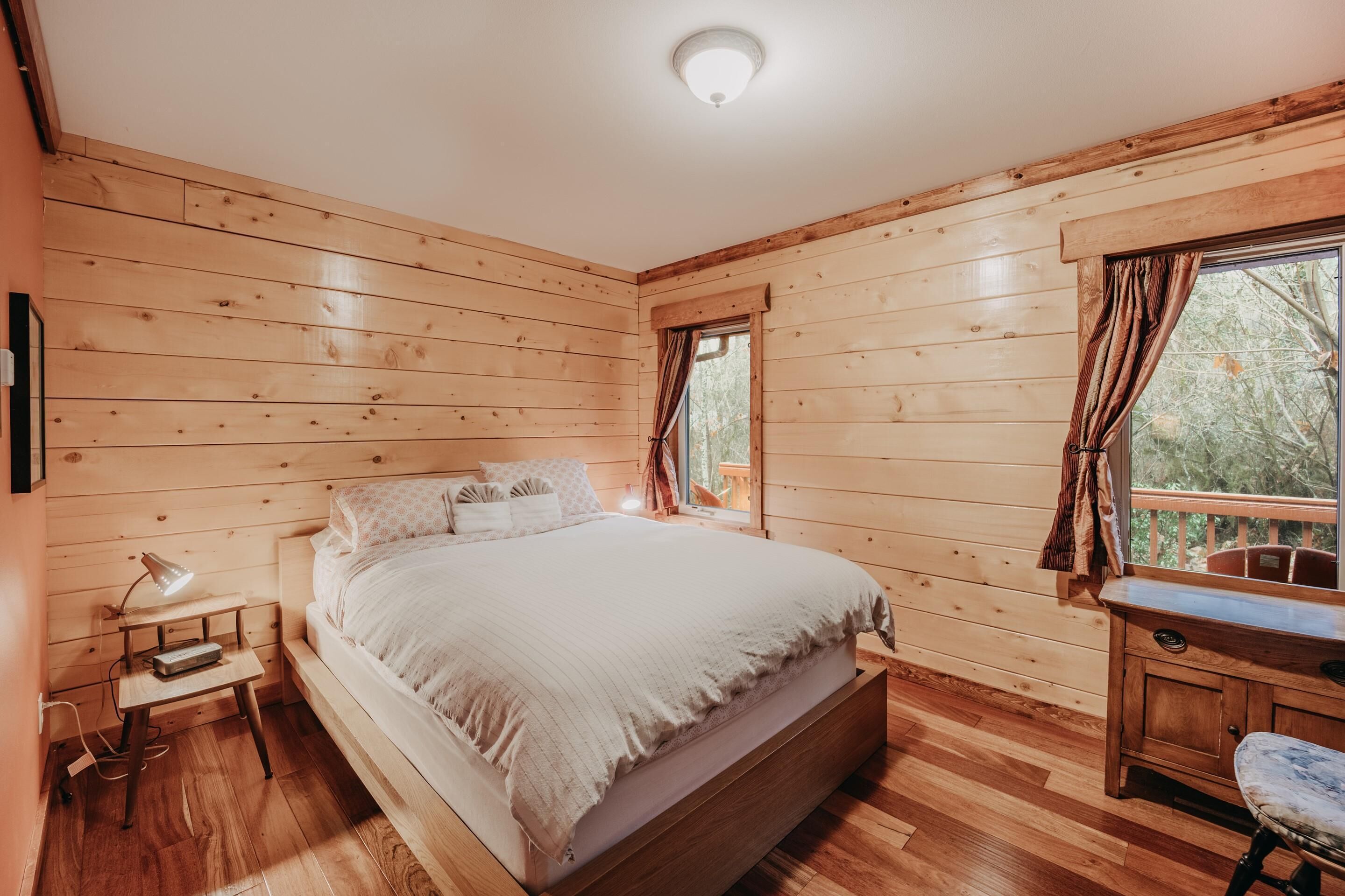 A wooden-paneled bedroom with a bed, bedside table, lamp, and a window with curtains.