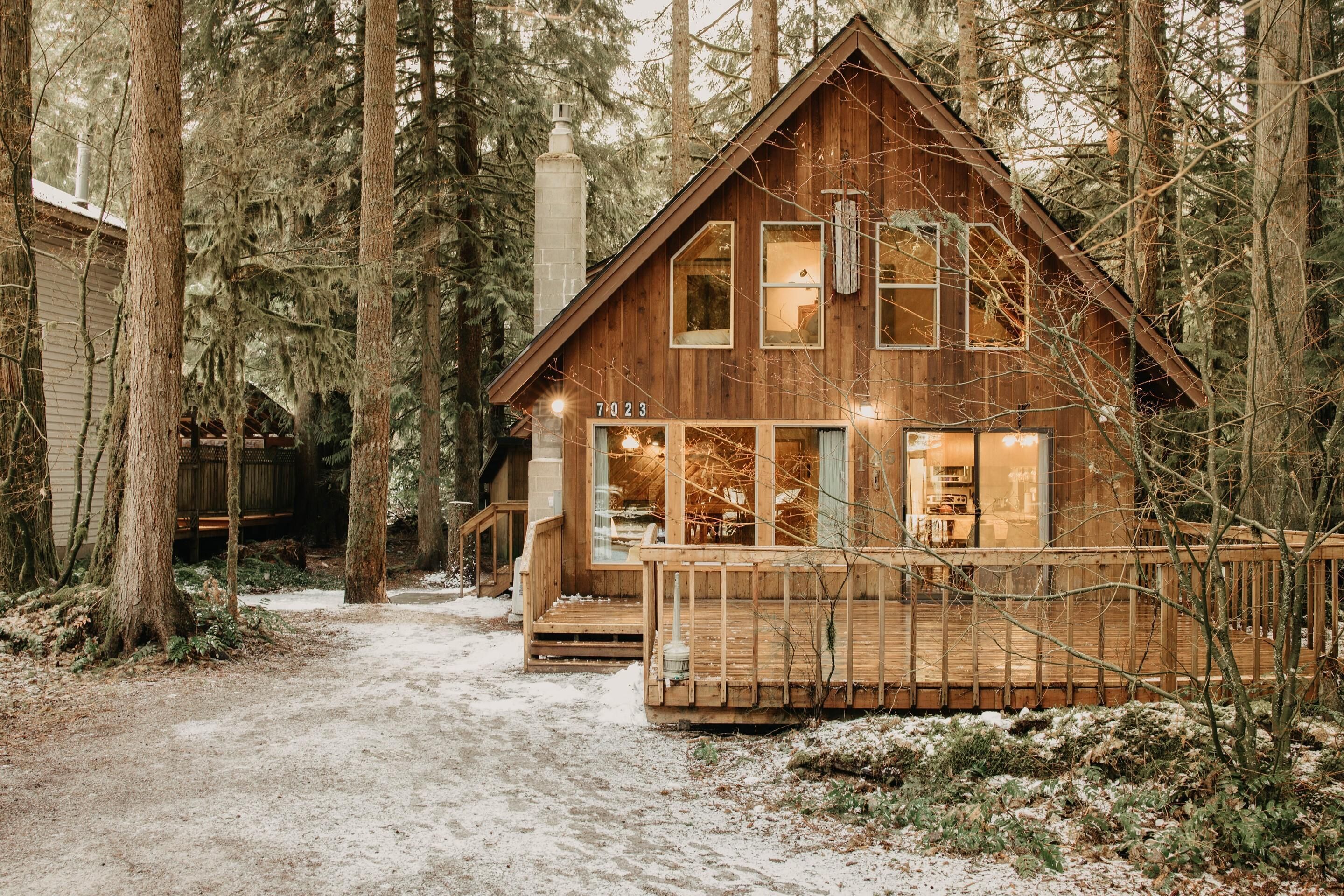 A wooden cabin with a number 7023, surrounded by tall trees and a snow-covered path.